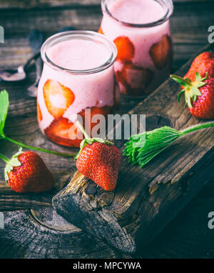 Une fraise rouge mûr et deux pots en verre de smoothies sur une table en bois gris Banque D'Images