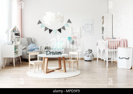 Bannière et lampe au-dessus d'une petite table avec des chaises dans des chambre de l'enfant avec des meubles blancs et des jouets Banque D'Images