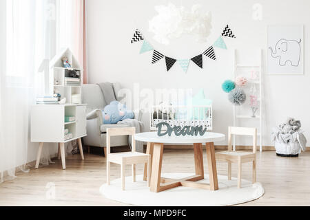 Bannière et lampe au-dessus d'une petite table avec des chaises en blanc chambre d'enfant avec pompons pastel sur l'échelle Banque D'Images