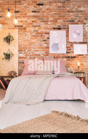 Chambre à coucher moderne avec lit double, literie rose et mur de brique Banque D'Images