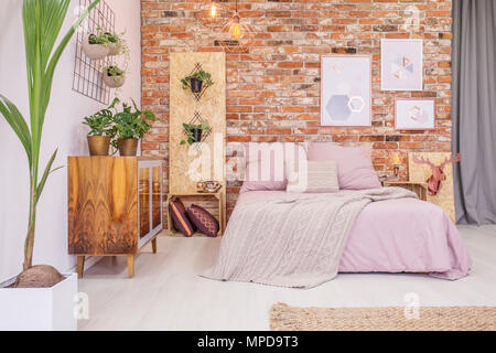 Chambre avec lit double, mur de brique et vert plantes décoratives Banque D'Images
