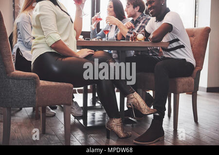 Fille de flirter avec un mec de toucher le pied de la jambe sous la table dans un café tout en s'amusant avec des amis. Le flirt avec le pied pendant le déjeuner Banque D'Images