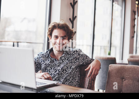 Beau jeune homme assis au bureau avec tasse de café et de travail sur le projet cyber moderne technologies. Businessman with notebook en essayant de garder dans la sphère du marketing numérique Date limite Banque D'Images