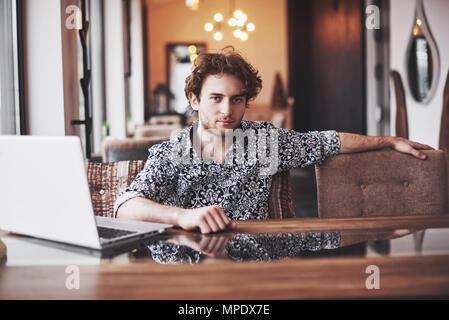 Beau jeune homme assis au bureau avec tasse de café et de travail sur le projet cyber moderne technologies. Businessman with notebook en essayant de garder dans la sphère du marketing numérique Date limite Banque D'Images