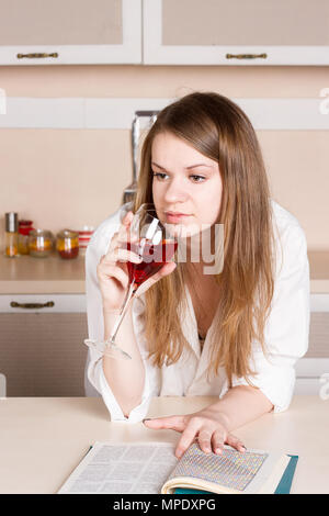 Fille aux longs cheveux en shirt dans la cuisine avec un verre de vin rouge Banque D'Images