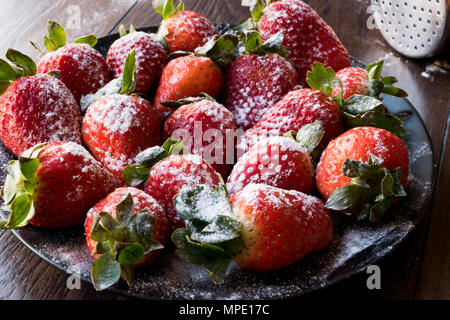 Produits frais bio fraise mûre avec du sucre en poudre sur la plaque noire. L'alimentation biologique. Banque D'Images