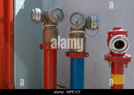 Old vintage, bouches d'incendie avec des trous ronds pour flexibles de raccordement, grues, peint en rouge et bleu, contre un mur blanc arrière-plan. Banque D'Images