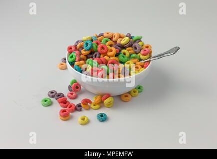 Un bol rempli de sucre saveur fruitée générique enrobés de céréales de petit déjeuner avec du lait et une cuillère dans l'aliment et de céréales renversé sur une table. Banque D'Images