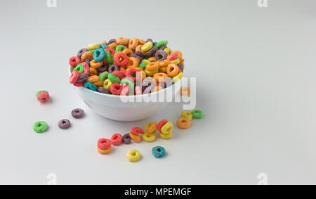 Un bol rempli de dragées aux génériques de céréales de petit déjeuner à saveur fruitée avec du lait et céréales renversé sur une table. Banque D'Images
