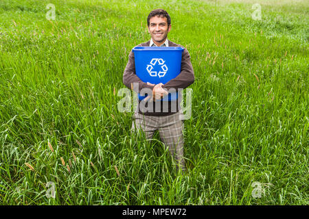 Un homme debout dans un champ d'herbe verte et des arbres tenant une corbeille. Un effet positif de conceptuel le recyclage. Banque D'Images