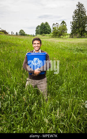 Un homme debout dans un champ d'herbe verte et des arbres tenant une corbeille. Un effet positif de conceptuel le recyclage. Banque D'Images