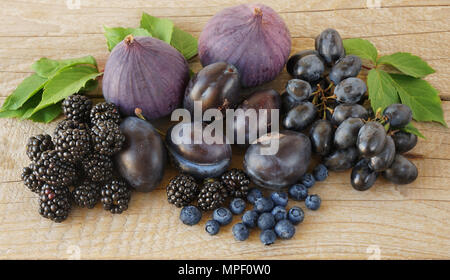 Bleu et violet de la nourriture. Les mûres, raisins, prunes, myrtilles, des figues sur un fond de bois. Savoureux et les fruits mûrs et les petits fruits. Banque D'Images