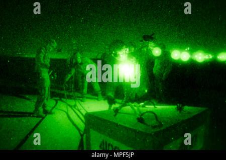 Les soldats de l'armée américaine et portugais affectés au groupement tactique multinational est mènent des opérations de nuit de chargement d'élingue au camp Bondsteel, Kosovo, le 16 février. Les soldats utilisent des lunettes de vision nocturne pour attacher des blocs de béton à un Black Hawk UH-60 stationnaire, piloté par des aviateurs de l'armée américaine. La formation simule la livraison de fournitures et de véhicules aux positions avancées, appuyant les missions de la KFOR et assurant la sûreté et la sécurité des opérations. Le Black Hawk est propulsé par deux turbomoteurs General Electric T700-GE-701C, capables de soulever des cargaisons et du personnel pendant les opérations nocturnes. Banque D'Images