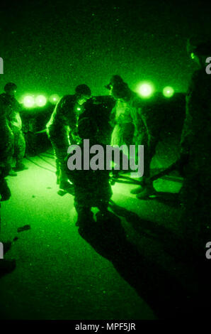 Des soldats de l'armée américaine et des forces portugaises affectés au groupement tactique multinational-est se préparent pour des opérations de chargement de nuit à l'élingue au camp Bondsteel, Kosovo, le 16 février. À l'aide de lunettes de vision nocturne, ils attachent des blocs de béton à un hélicoptère UH-60 Black Hawk pour pratiquer le levage de marchandises et de véhicules pour être opérationnel. L'exercice améliore la coordination, la maîtrise du vol de nuit et l'efficacité de la mission. L'UH-60 est équipé de deux turbopropulseurs General Electric T700, capables d'effectuer des missions de portage tactique pour les opérations de la KFOR. Banque D'Images