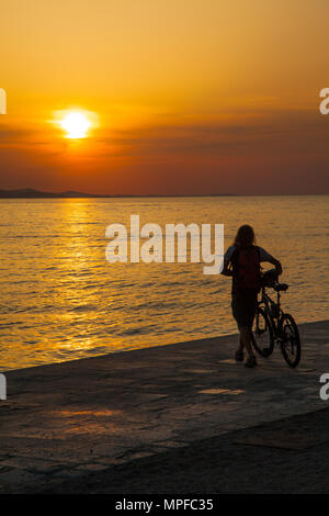 L'homme avec le vélo en regardant belle rouge et orange d'or glorieux dynamique vives coucher de soleil sur la mer au port de Zadar sur la côte Adriatique Croatie Banque D'Images