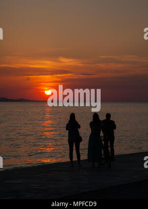 Regarder les gens beaux golden glorieuse et rouge vif orange vibrant coucher de soleil sur la mer au port de Zadar sur la côte Adriatique Croatie Banque D'Images