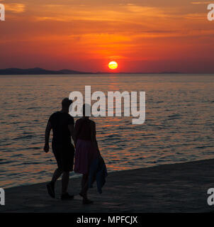 Regarder les gens beaux golden glorieuse et rouge vif orange vibrant coucher de soleil sur la mer au port de Zadar sur la côte Adriatique Croatie Banque D'Images