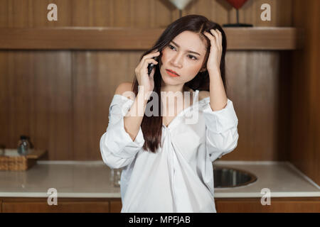 Les jeunes mécontents Woman talking on mobile phone in kitchen Banque D'Images