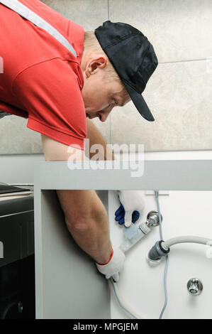 Installation d'appareils ménagers. Workman attache un tuyau d'eau à la vanne. Banque D'Images