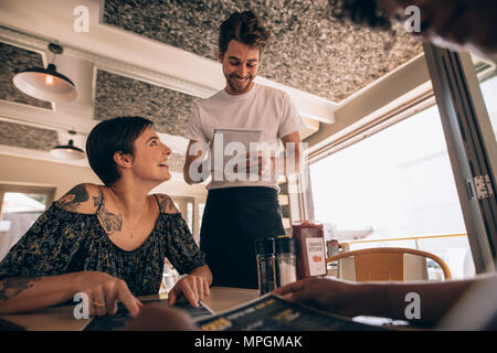 Femme parlant de serveur au restaurant. Jeune femme assise au café avec waiter taking order. Banque D'Images