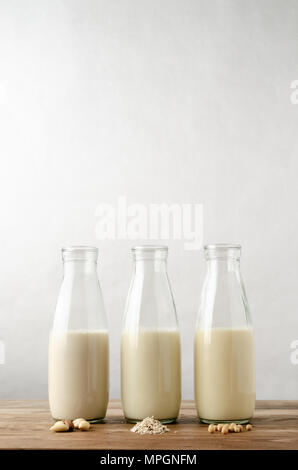 Une rangée de trois bouteilles en verre contenant des produits laitiers le lait de remplacement. Ingrédient clé en avant-plan sur les planches en bois table. L'avoine, d'amande et de soja varieti Banque D'Images