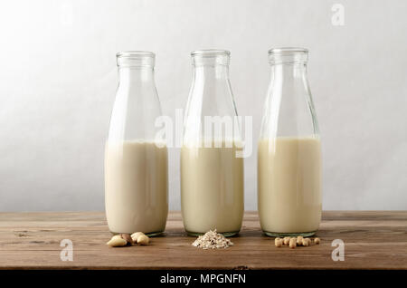 Rangée de trois bouteilles en verre contenant des produits laitiers boissons substituts du lait maternel. Ingrédients clés d'amandes ; l'avoine et le soja en avant-plan sur les planches de bois Banque D'Images