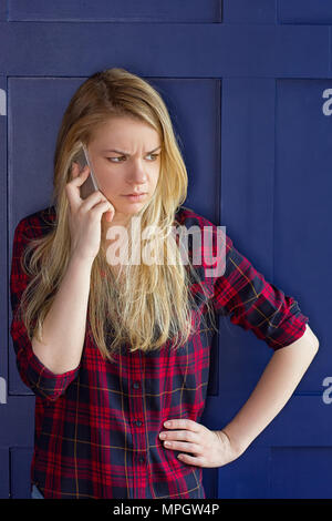 Jolie femme appeler quelqu'un par téléphone portable en souriant à la caméra contre mur bleu Banque D'Images