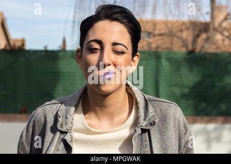 Belle jeune fille de race blanche aux cheveux courts posant dans un shoot avec la mode des vêtements modernes. Elle est assise sur une chaise sur l'herbe. Banque D'Images