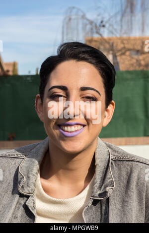 Belle jeune fille de race blanche aux cheveux courts posant dans un shoot avec la mode des vêtements modernes. Elle est assise sur une chaise sur l'herbe. Banque D'Images