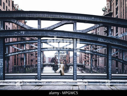 Vue arrière de woman wearing long manteau debout sur le pont dans le vieux quartier d'entrepôts Speicherstadt à Hambourg Banque D'Images