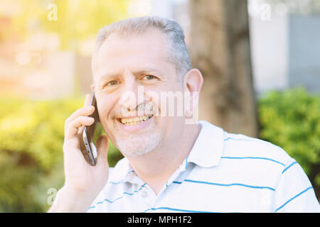 Bel homme d'âge moyen à parler au téléphone dans un parc. À l'extérieur. Technologie concept. Banque D'Images