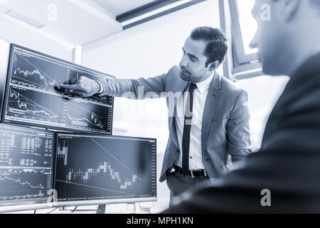 Les stocks commerciaux d'affaires en ligne. Les courtiers en regardant des graphiques, des index et des chiffres sur plusieurs écrans d'ordinateur. Collègues de discussion en trad Banque D'Images