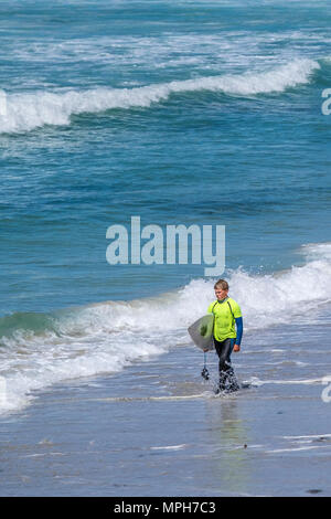 Un jeune surfer carrying his surfboard et marcher le long du rivage à Sennen Cove, à Cornwall. Banque D'Images