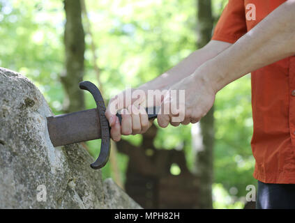 Deux mains d'un garçon prend une épée magique appelée Excalibur dans la forêt de Camelot Banque D'Images