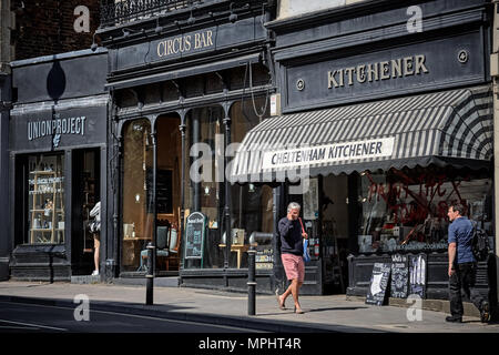 Les piétons circulant le long de la rue à l'extérieur de la façade noir boutiques et bars sur la promenade près de Montpellier, Cheltenham, Gloucestershire. Banque D'Images