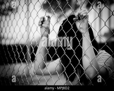 Le noir et blanc de femmes Hands holding clôture sur un paysage extérieur en plein jour. Part en prison, concept de la prison à vie Banque D'Images