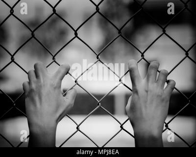 Le noir et blanc de femmes Hands holding clôture sur un paysage extérieur en plein jour. Part en prison, concept de la prison à vie Banque D'Images