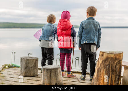 Trois amis jouer à la pêche sur la jetée en bois près de l'étang. Tout-petits deux garçons et une fille à la rivière. Les enfants s'amusant avec des bâtons de canne à pêche. Bac Banque D'Images