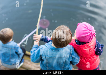 Trois amis jouer à la pêche sur la jetée en bois près de l'étang. Tout-petits deux garçons et une fille à la rivière. Les enfants s'amusant avec des bâtons de canne à pêche. Bac Banque D'Images