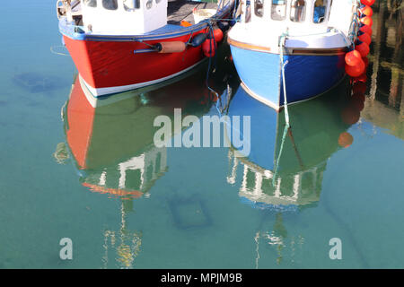 Close up de fronts d'un petit rouge et un petit homard bleu bateau dans port avec reflets d'arcs dans l'eau Banque D'Images