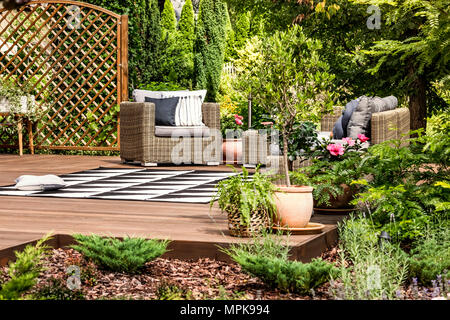 Meubles de jardin en rotin sur une terrasse ornée de plantes, arbustes, fleurs et arbres Banque D'Images