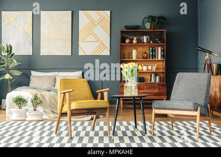 Chambre rétro intérieur avec des affiches ci-dessus lit, plantes, bibliothèque et deux chaises à côté d'une petite table sur le tapis Banque D'Images