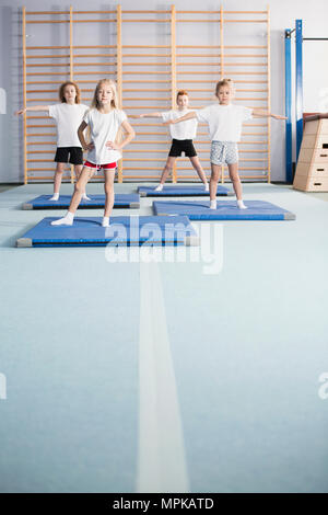 Les filles et les garçons de l'école faire exercices d'échauffement dans une salle de sport moderne avec l'intérieur des bars et des équipements de gymnastique mural Banque D'Images