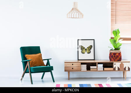 Buffet scandinave avec des livres et des décorations colorées et un fauteuil rétro dans un intérieur salon blanc Banque D'Images