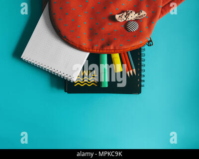 Les fournitures scolaires photo un sac à dos rose avec les ordinateurs portables, les marqueurs et l'pensils est couchée sur le bureau bleu Banque D'Images