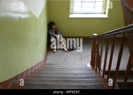 Adolescent assis au fond de l'ancien escalier. Banque D'Images