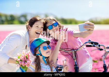 Dutch family riding bicycle in tulip champs de fleurs en Hollande. Mère et enfants en tenant photo selfies téléphone mobile avec appareil photo sur des vélos à blooming Banque D'Images