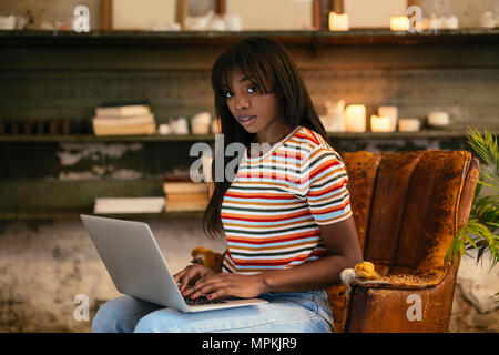 Portrait de jeune femme assise sur un vieux fauteuil en cuir working on laptop dans un loft Banque D'Images