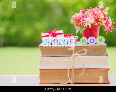 Concept de la fête des mères. Amour maman alphabet sur pile de livres, cadeaux, tasse de thé avec coeur rouge sur fond de fleurs et Banque D'Images