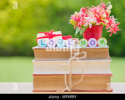 Concept de la fête des mères. Amour maman alphabet sur pile de livres, cadeaux, tasse de thé avec coeur rouge sur fond de fleurs et Banque D'Images